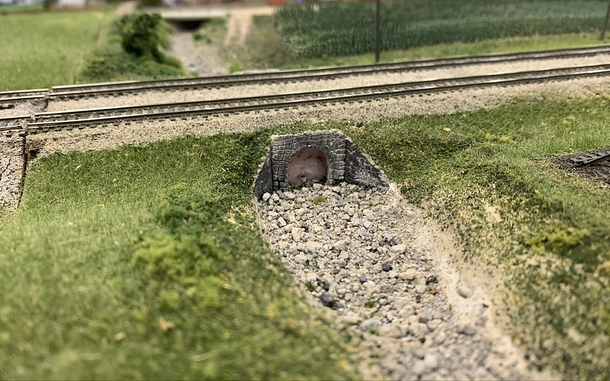 Dry rock-bed creek running through a culvert under the double main, with the lane bridge in the background